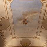 In una terza stanza ampie fasce bianche con bordure dorate, interrotte da ovali con fiori colorati, racchiudono uno sfondo celestiale...